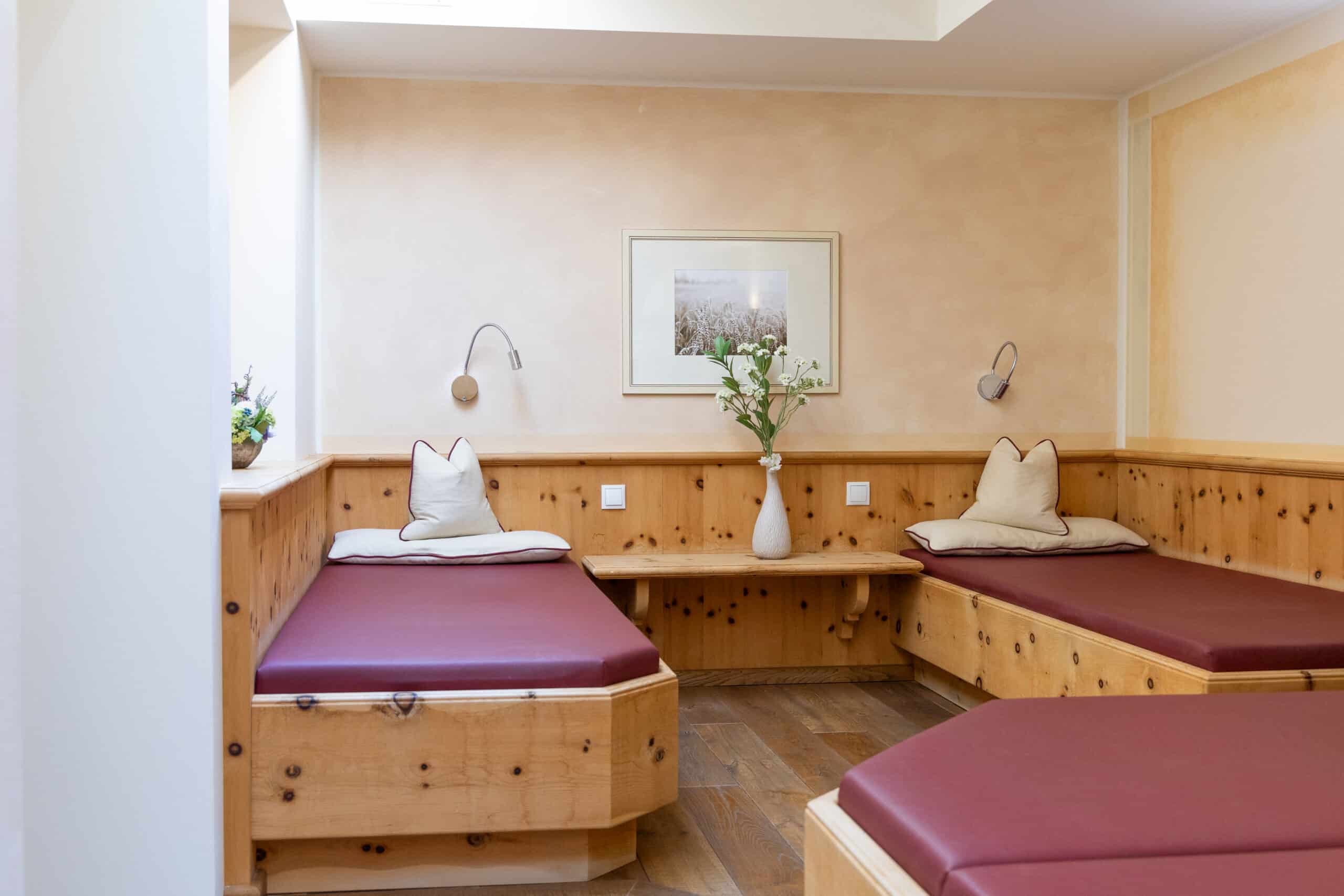 Ruhiger Ruheraum mit zwei Holzliegen, hellen W&auml;nden und einer Vase mit Blumen als Dekoration.