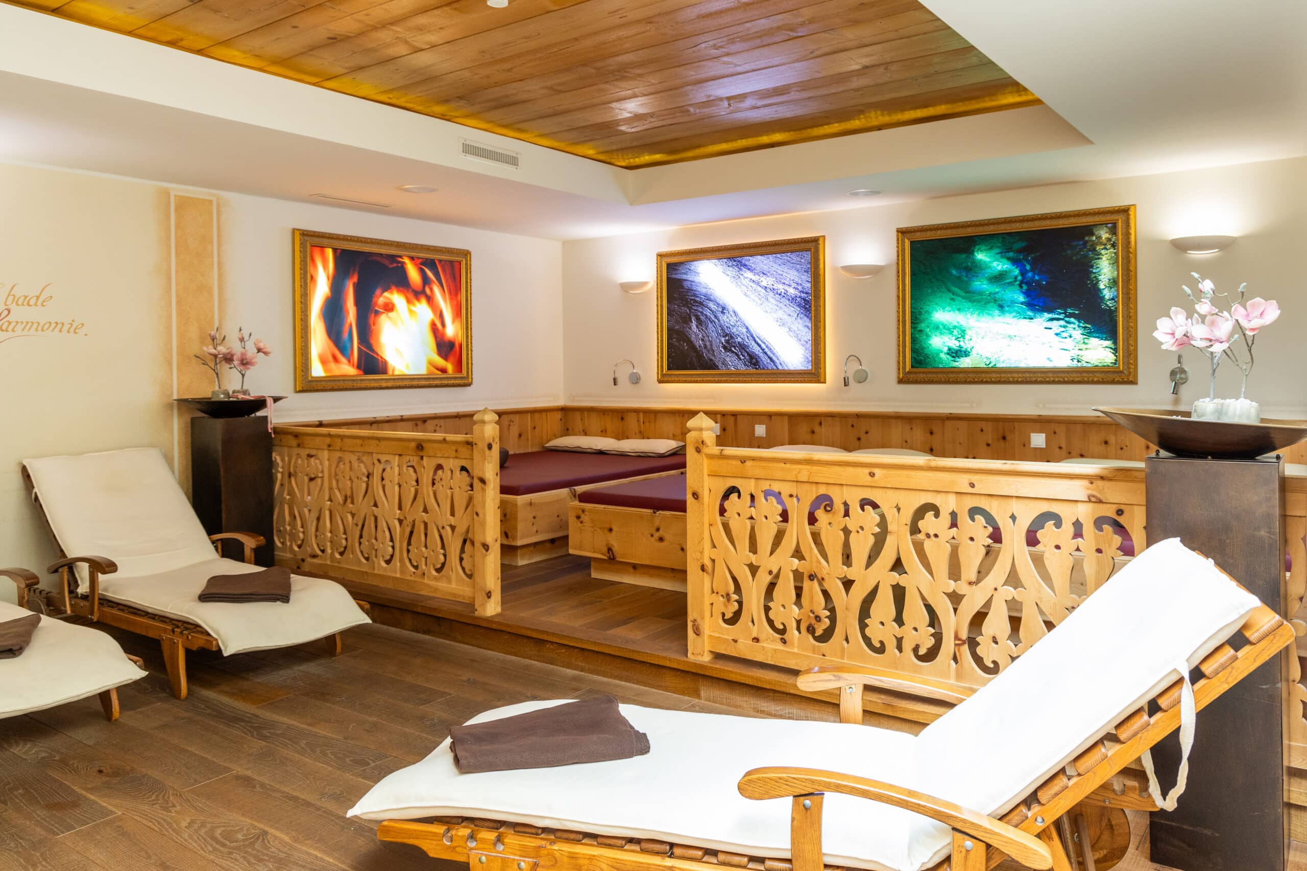 Gem&uuml;tlicher Wellness-Ruheraum mit Holzliegen, warmem Licht und dekorativen Bildern an den W&auml;nden.